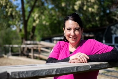 A picture of the founder, Rachael Hartline, at the farm on a sunny day leaning on a fence